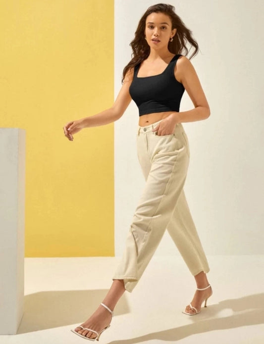 Woman wearing a black crop top and beige pants against a yellow and white background